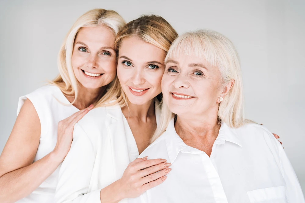 Three generations of beautiful women, facing the camera and smiling together.